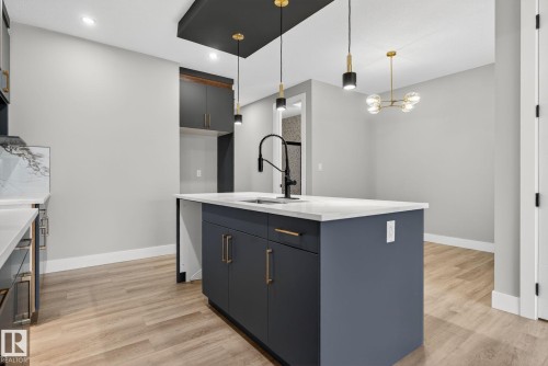 Kitchen with a kitchen island with sink, light wood finished floors, modern cabinets, light stone counters, and a chandelier - 456 Crystal Creek Link, Leduc, AB - Indoor Photo Showing Kitchen