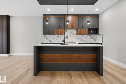 Kitchen with modern cabinets, light stone counters, an island with sink, light wood finished floors, and hanging light fixtures - 456 Crystal Creek Link, Leduc, AB - Indoor