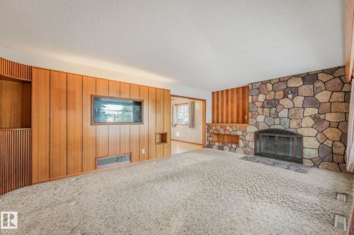 Unfurnished living room featuring wood walls, a stone fireplace, a textured ceiling, and carpet flooring - 10324 42 Street, Edmonton, AB - Indoor With Fireplace