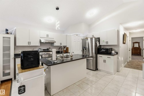 Kitchen with white cabinets, pendant lighting, lofted ceiling, a kitchen island with sink, and stainless steel appliances - 1706 Turvey Bend, Edmonton, AB - Indoor Photo Showing Kitchen With Stainless Steel Kitchen With Double Sink