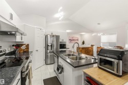 Kitchen featuring stainless steel appliances, white cabinets, vaulted ceiling, light tile patterned floors, and an island with sink - 