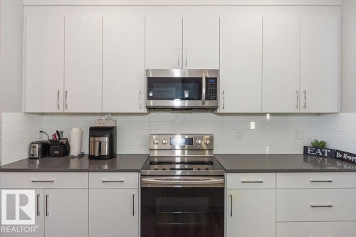 Kitchen with stainless steel appliances, white cabinetry, tasteful backsplash, and dark stone countertops - 1224 Mcconachie Boulevard, Edmonton, AB - Indoor Photo Showing Kitchen With Upgraded Kitchen