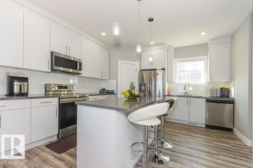 Kitchen featuring stainless steel appliances, a breakfast bar area, a kitchen island, white cabinets, and dark wood-style floors - 1224 Mcconachie Boulevard, Edmonton, AB - Indoor Photo Showing Kitchen With Upgraded Kitchen