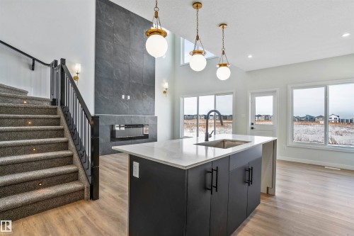 Kitchen with an island with sink, a high ceiling, a tiled fireplace, decorative light fixtures, and light wood-style floors - 112 25 Street, Edmonton, AB - Indoor Photo Showing Kitchen