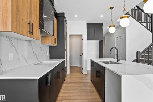 Dual tone kitchen with two tone color scheme, light stone counters, a center island with sink, modern cabinets, and light wood-style floors - 112 25 Street, Edmonton, AB - Indoor Photo Showing Kitchen With Upgraded Kitchen