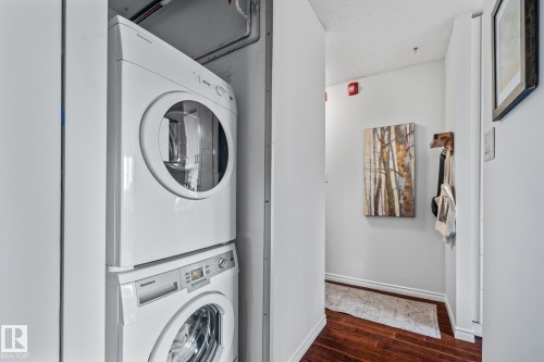 Laundry area featuring stacked washing machine and dryer, dark wood finished floors, and a textured ceiling - 1502 9909 110 Street, Edmonton, AB - Indoor Photo Showing Laundry Room
