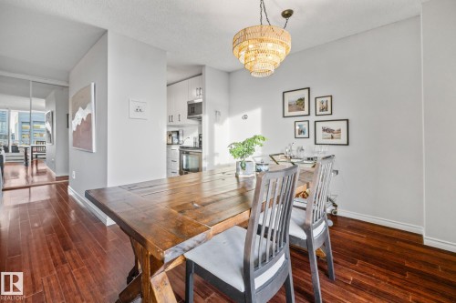 Dining area with a chandelier, dark wood-type flooring, and a textured ceiling - 1502 9909 110 Street, Edmonton, AB - Indoor Photo Showing Dining Room