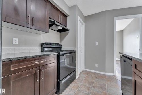 Kitchen with black electric range oven, dark wood finish cabinets, dishwasher, and light stone counters - 216 5804 Mullen Place, Edmonton, AB - Indoor Photo Showing Kitchen