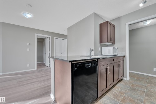 Kitchen with black dishwasher, dark wood finish cabinets, a peninsula, and white microwave - 216 5804 Mullen Place, Edmonton, AB - Indoor