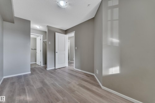 Unfurnished bedroom featuring a spacious closet, light wood-style floors, and a textured ceiling - 216 5804 Mullen Place, Edmonton, AB - Indoor Photo Showing Other Room