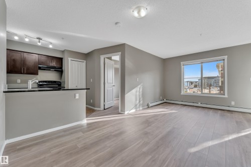 Unfurnished living room featuring light wood-type flooring, a textured ceiling, and baseboard heating - 216 5804 Mullen Place, Edmonton, AB - Indoor Photo Showing Kitchen