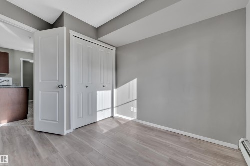 Unfurnished bedroom with light wood-style flooring, baseboard heating, and a closet - 216 5804 Mullen Place, Edmonton, AB - Indoor Photo Showing Other Room