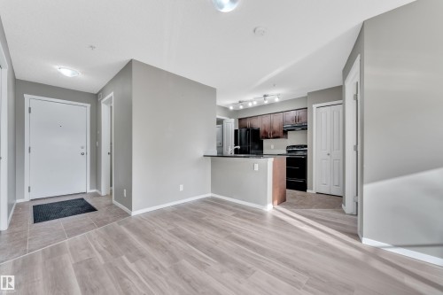 Kitchen featuring dark wood finish cabinets, black appliances, a peninsula, light wood-type flooring, and dark countertops - 216 5804 Mullen Place, Edmonton, AB - Indoor Photo Showing Kitchen