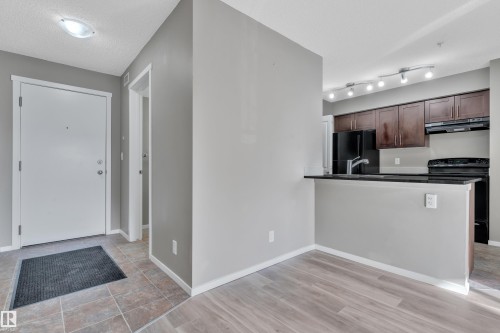 Kitchen with black appliances, a peninsula, dark wood finish cabinets, light wood finished floors, and a textured ceiling - 216 5804 Mullen Place, Edmonton, AB - Indoor Photo Showing Kitchen