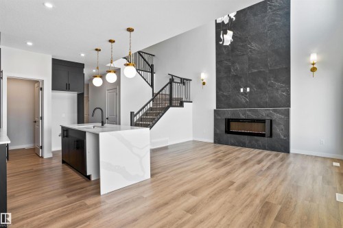 Kitchen with a kitchen island with sink, decorative light fixtures, light stone countertops, modern cabinets, and light wood finished floors - 116 25 Street, Edmonton, AB - Indoor With Fireplace