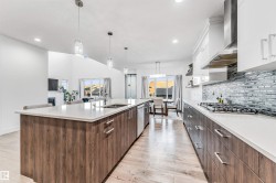 Kitchen with decorative light fixtures, light wood-style flooring, two tone cabinets, a large island, and light stone counters - 