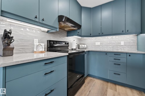 Kitchen featuring black / electric stove, range hood, light stone countertops, light wood-type flooring, and blue cabinetry - 9215 Ottewell Road, Edmonton, AB - Indoor Photo Showing Kitchen