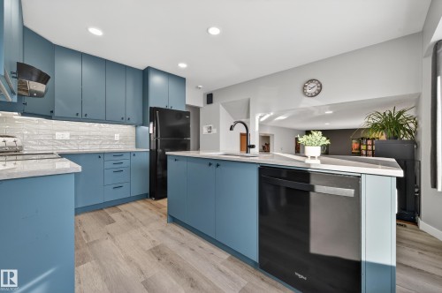 Kitchen with black appliances, blue cabinetry, light stone counters, backsplash, and ventilation hood - 9215 Ottewell Road, Edmonton, AB - Indoor Photo Showing Kitchen With Upgraded Kitchen