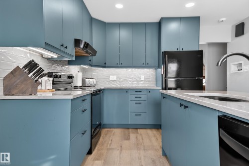 Kitchen featuring black appliances, light stone countertops, blue cabinetry, light wood-style floors, and backsplash - 9215 Ottewell Road, Edmonton, AB - Indoor Photo Showing Kitchen With Upgraded Kitchen