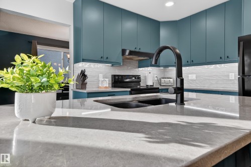 Kitchen featuring light stone countertops, black appliances, backsplash, blue cabinets, and range hood - 9215 Ottewell Road, Edmonton, AB - Indoor Photo Showing Kitchen With Double Sink With Upgraded Kitchen