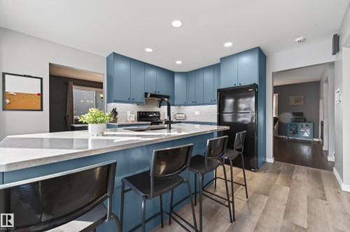 Kitchen featuring blue cabinets, a breakfast bar area, black appliances, light wood-type flooring, and light stone countertops - 9215 Ottewell Road, Edmonton, AB - Indoor Photo Showing Kitchen With Upgraded Kitchen