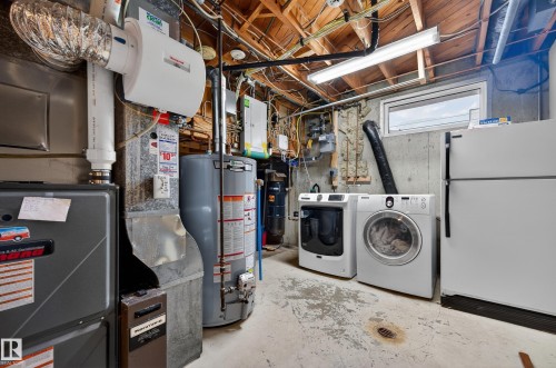Laundry area featuring heating unit, gas water heater, washer and dryer, unfinished concrete flooring, and electric panel - 9215 Ottewell Road, Edmonton, AB - Indoor Photo Showing Laundry Room