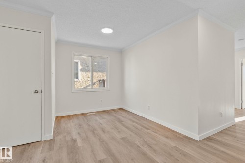 Empty room with light wood-style flooring, a textured ceiling, and ornamental molding - 4631 126 Avenue, Edmonton, AB - Indoor Photo Showing Other Room