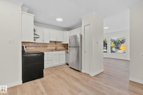 Kitchen featuring stainless steel appliances, white cabinets, ornamental molding, light wood-style flooring, and decorative backsplash - 4631 126 Avenue, Edmonton, AB - Indoor Photo Showing Kitchen
