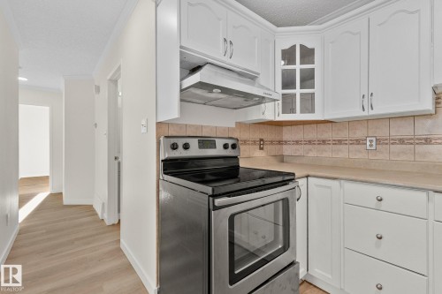 Kitchen featuring stainless steel electric stove, white cabinets, glass insert cabinets, ventilation hood, and light countertops - 4631 126 Avenue, Edmonton, AB - Indoor Photo Showing Kitchen