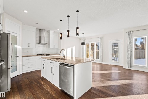 Kitchen featuring light stone countertops, dark wood-style flooring, an island with sink, and stainless steel appliances - 2036 Ainslie Link Link, Edmonton, AB - Indoor Photo Showing Kitchen With Upgraded Kitchen