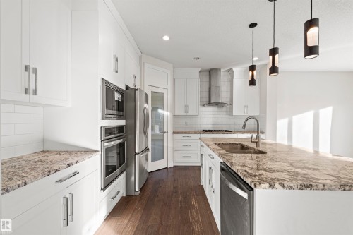 Kitchen with light stone countertops, white cabinets, an island with sink, and stainless steel appliances - 2036 Ainslie Link Link, Edmonton, AB - Indoor Photo Showing Kitchen With Double Sink With Upgraded Kitchen