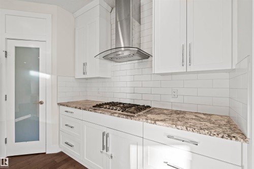 Kitchen featuring white cabinetry, dark wood-style flooring, tasteful backsplash, and light stone countertops - 2036 Ainslie Link Link, Edmonton, AB - Indoor Photo Showing Kitchen With Upgraded Kitchen