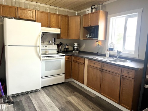 Kitchen featuring wood finish cabinets, white appliances, dark wood-style flooring, dark countertops, and wood ceiling - 4811 48 Ave, Evansburg, AB - Indoor Photo Showing Kitchen With Double Sink