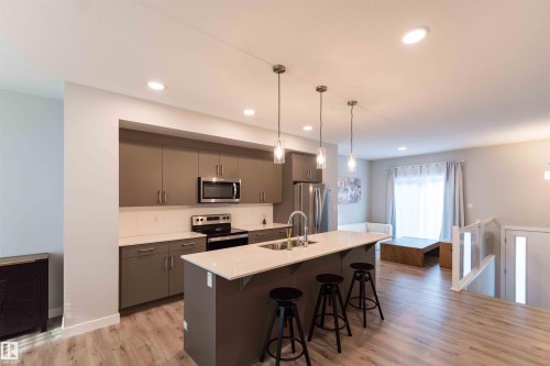 Kitchen with a kitchen breakfast bar, stainless steel appliances, hanging light fixtures, light wood-style floors, and a kitchen island with sink - 21 1729 Keene Crescent, Edmonton, AB - Indoor Photo Showing Kitchen With Double Sink With Upgraded Kitchen