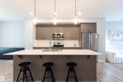 Kitchen with a breakfast bar, gray cabinetry, hanging light fixtures, light wood-style flooring, and stainless steel appliances - 21 1729 Keene Crescent, Edmonton, AB - Indoor Photo Showing Kitchen With Upgraded Kitchen