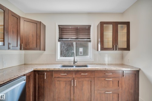 Kitchen with glass insert cabinets, wood finish cabinetry, stainless steel dishwasher, and light stone countertops - 6803 112A Street, Edmonton, AB - Indoor Photo Showing Kitchen With Double Sink