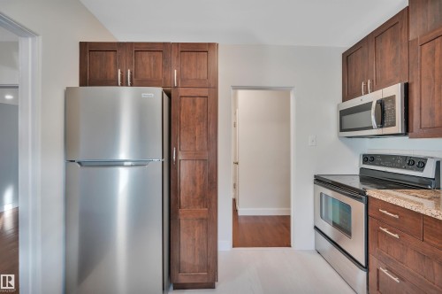 Kitchen featuring stainless steel appliances, light stone countertops, and light wood-style floors - 6803 112A Street, Edmonton, AB - Indoor Photo Showing Kitchen