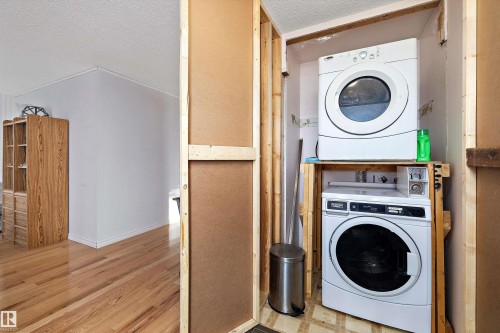 Laundry area with a textured ceiling, stacked washing machine and dryer, and light wood-style floors - 12117 91 Street, Edmonton, AB - Indoor Photo Showing Laundry Room