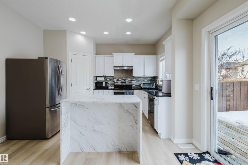 Kitchen featuring white cabinetry, stainless steel appliances, dark stone countertops, tasteful backsplash, and light wood finished floors - 8420 Sloane Crescent, Edmonton, AB - Indoor Photo Showing Kitchen