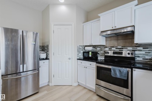 Kitchen featuring stainless steel appliances, white cabinetry, light wood-style floors, backsplash, and dark stone countertops - 8420 Sloane Crescent, Edmonton, AB - Indoor Photo Showing Kitchen With Upgraded Kitchen