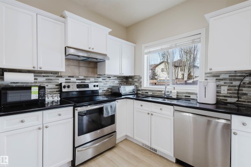 Kitchen with stainless steel appliances, white cabinets, light wood finished floors, and backsplash - 8420 Sloane Crescent, Edmonton, AB - Indoor Photo Showing Kitchen With Double Sink