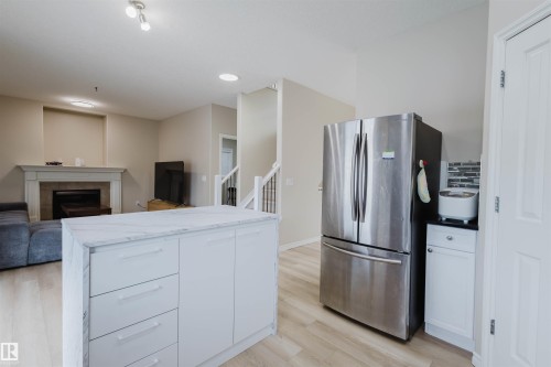 Kitchen featuring freestanding refrigerator, open floor plan, a tile fireplace, light wood-type flooring, and white cabinets - 8420 Sloane Crescent, Edmonton, AB - Indoor With Fireplace