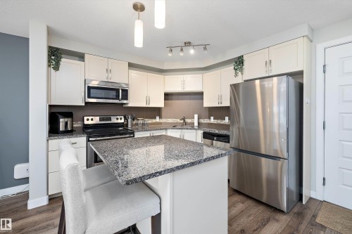 Kitchen featuring stainless steel appliances, pendant lighting, dark stone countertops, a breakfast bar, and a center island - 205 8515 99 Street, Edmonton, AB - Indoor Photo Showing Kitchen With Stainless Steel Kitchen With Upgraded Kitchen