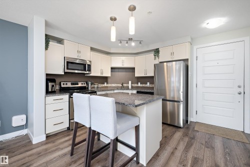 Kitchen with stainless steel appliances, hanging light fixtures, a breakfast bar area, white cabinets, and a kitchen island - 205 8515 99 Street, Edmonton, AB - Indoor Photo Showing Kitchen With Stainless Steel Kitchen With Upgraded Kitchen