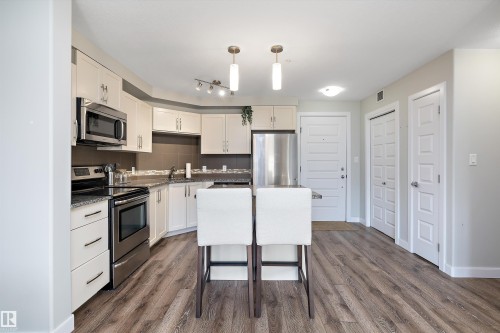 Kitchen featuring stainless steel appliances, pendant lighting, white cabinetry, dark wood finished floors, and a kitchen breakfast bar - 205 8515 99 Street, Edmonton, AB - Indoor Photo Showing Kitchen With Stainless Steel Kitchen With Upgraded Kitchen