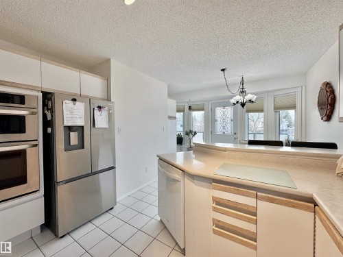 Kitchen featuring stainless steel appliances, light countertops, a textured ceiling, white cabinets, and suspended lighting - 3772 30 Street, Edmonton, AB - Indoor Photo Showing Kitchen