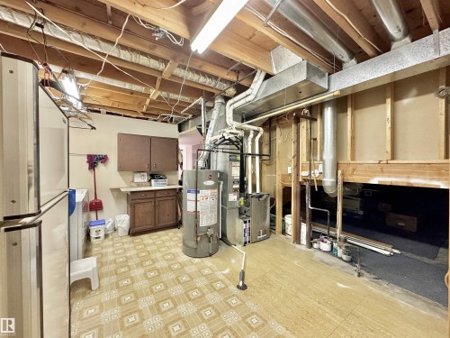 Unfinished basement featuring light floors, water heater, freestanding refrigerator, and heating unit - 3772 30 Street, Edmonton, AB - Indoor Photo Showing Basement