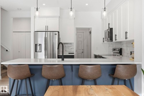 Dual tone kitchen featuring a kitchen bar, stainless steel appliances, a peninsula, hanging light fixtures, and two tone cabinetry - 16627 31 Avenue, Edmonton, AB - Indoor Photo Showing Kitchen With Upgraded Kitchen