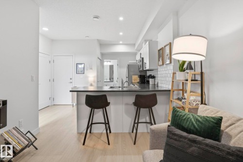 Kitchen featuring a kitchen bar, a peninsula, light wood-style flooring, tasteful backsplash, and dark countertops - 16627 31 Avenue, Edmonton, AB - Indoor