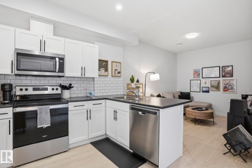 Kitchen with a peninsula, stainless steel appliances, white cabinetry, dark countertops, and open floor plan - 16627 31 Avenue, Edmonton, AB - Indoor Photo Showing Kitchen With Double Sink With Upgraded Kitchen